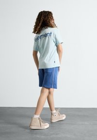 Camiseta de manga corta azul claro con el logo "element" en la parte trasera, combinada con pantalones cortos azules y zapatillas altas beige.