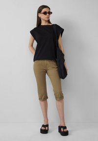 Czarny, krótki top z szerokimi ramionami; khaki spodnie typu cropped; czarne sandały na platformie; teksturowana czarna torba na ramię; okrągłe okulary przeciwsłoneczne.