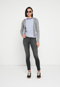 Gray zip-up hoodie over a blue-striped short-sleeve shirt, paired with dark skinny jeans and black shoes with white laces.