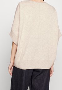 Beige übergroßer Strickpullover mit kurzen Ärmeln, geripptem Saum und lässiger Passform. Glatte Textur mit feinen Nähdetails auf der Rückseite.