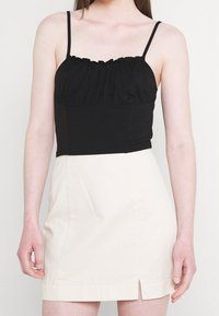 Černý top bez rukávů s volánovým výstřihem, doplněný o upnutou krémovou mini sukni s předním rozparkem a hladkou texturou.