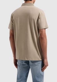 Beige polo shirt met korte mouwen en een kraag, met een subtiele textuur en een klein logo op de rug. Gecombineerd met lichte denim jeans.