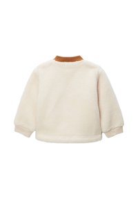 Veste en polaire crème avec un col et des poignets marron, présentant une texture douce et une coupe décontractée, idéale pour un look casual.