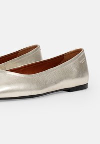 Sølv metallisk ballet flats med en glatt, teksturert finish, lav svart hæl og brun innersåle. Minimalistisk slip-on design.