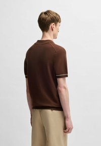 Brun kortärmad polo tröja med en strukturerad tyg och en kontrasterande ljus kant på ärmarna, designad med en klassisk krage.