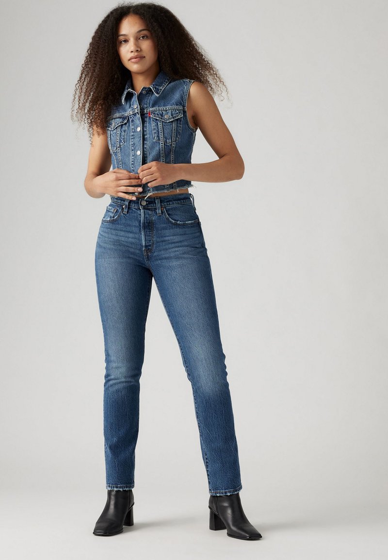 Chaleco de denim con diseño sin mangas, lavado claro y bolsillos frontales, combinado con jeans de pierna recta de talle alto en denim azul a juego.
