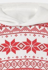 Stickad tröja med vikbar vit krage. Har ett röd- och vitt mönster med snöflingor och geometriska former över hela kroppen.