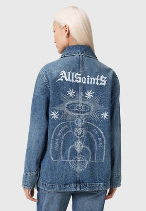 Henkilö, jolla on platinaa vaaleat hiukset, pukeutunut siniseen farkkutakkiin, jossa on valkoinen AllSaints-logo ja taidokas taivaankappaleiden kuvio takana.