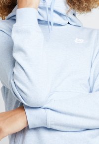 Ljusblå hoodie i mjukt tyg med dragsko i huvan och vitt Nike-logotyp på bröstet. Har ribbade muddar och en avslappnad passform.