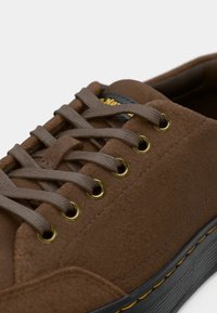 Barna velúr sportcipő aranyszínű fémfülekkel és szürke cipőfűzőkkel, fekete gumitalppal, melyet sárga díszcsík szegélyez.