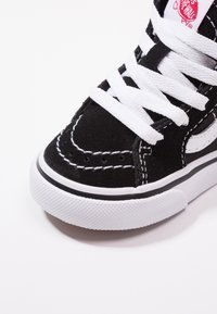 Schwarze Wildleder-Sneaker mit weißen Schnürsenkeln. Verfügt über eine weiße Gummisohle, kontrastierende Nähte und ein seitliches Logo-Element. Nahaufnahme des Zehenbereichs.