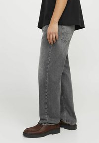 Grå denimjeans med rak passform, sydda detaljer och bakfickor, kombinerade med bruna läderskor på en neutral bakgrund.