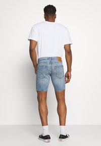 Světle modré džíny šortky se střihovým střihem, s klasickými zadními kapsami a hnědým koženým štítkem v pase, nošené s bílým tričkem.