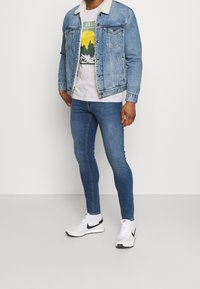 Chaqueta vaquera con cuello de piel sintética, azul claro, combinada con una camiseta gráfica y jeans ajustados azul oscuro, completada con zapatillas blancas Nike.