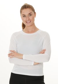 Pitkähihainen valkoinen urheiluvaate, joka on valmistettu kevyestä ja hengittävästä kankaasta. Mallissa on pyöreä pääntie sekä huomaamaton logo yksityiskohtana rinnassa.