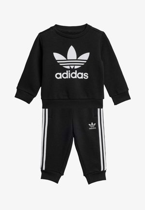 Musta puuvilla urheilutakki pitkähihaisilla hihoilla ja housuilla, jossa on valkoinen Adidas-logo ja kolme valkoista raitaa sivuilla.