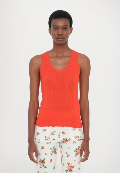 Red ribbed tank top with a scoop neckline, featuring a fitted shape. Paired with white floral-patterned trousers.