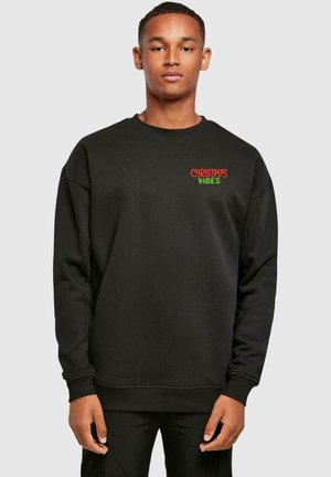 Black sweatshirt featuring "CHRISTMAS VIBES" in red and green on the chest. Made from soft material with a relaxed fit and ribbed cuffs.