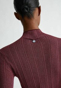 Viininpunainen ribbineulepaita korkealla kauluksella ja pienellä metallisella yksityiskohdalla takana. Kangas on hieman kiiltävä.