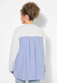 Sudadera gris con la parte trasera plisada a rayas azules y blancas, con escote redondo y mangas largas. Tejido suave y texturizado.