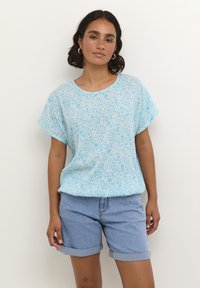 Top corto a maniche corte floreale blu chiaro realizzato in tessuto morbido, con una vestibilità rilassata e scollo rotondo, abbinato a pantaloni shorts in denim arrotolati.