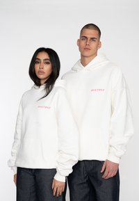 Sudaderas blancas con bolsillos frontales y capuchas grandes. Logo "MULTIPLY" en rosa en el pecho. Tejido suave con puños y dobladillo acanalados.