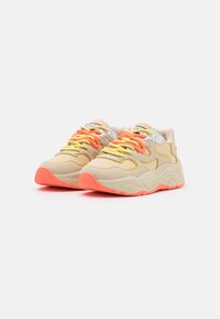Beige sneakers featuring a textured fabric upper, neon yellow and orange laces, and a chunky white midsole with a bright orange outsole.
