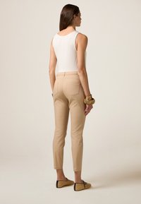 Mouwloze top in het wit, slim-fit beige broek met achterzakken en geweven tan platte schoenen met zwarte accenten. Gladde textuur van de stof in het geheel.