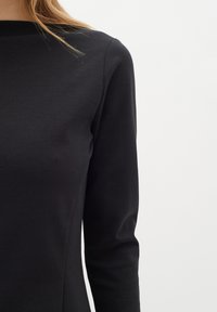 Czarna bluzka z długim rękawem i okrągłym dekoltem, wykonana z gładkiego materiału. Posiada dopasowany krój oraz proste szwy. Prosty i minimalistyczny design.