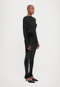 Long-sleeve black top paired with black high-waisted leggings, featuring a smooth texture and hand openings, complemented by pointed black heels.