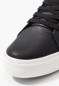 Mustat nahkakengät, joissa on teksturoitu pinta, valkoinen kumipohja, jossa on urakuvio, ja mustat nauhat. Lähikuva varvasalueesta.