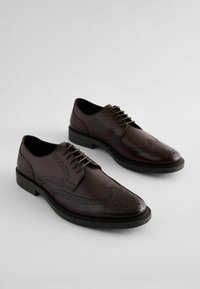 Souliers habillés en cuir marron à lacets avec des détails en brogue, texture lisse, bout arrondi et une semelle noire contrastante.