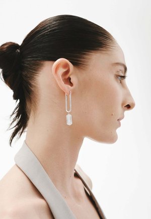 Pendientes de plata con un alambre largo y fino y un colgante rectangular con un patrón geométrico texturizado. Diseño elegante y moderno.