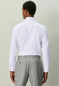 Hellviolettes gestreiftes Hemd mit langen Ärmeln, sichtbaren Manschetten mit Knöpfen und spitzem Kragen, kombiniert mit grauen gemusterten Hosen.