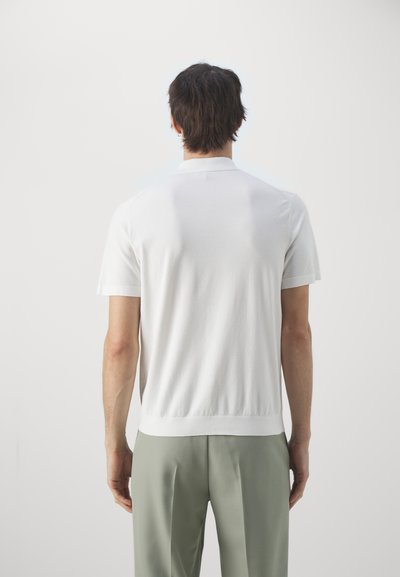 Hvit kortermet polo skjorte i strikket tekstur, med krage og rett kant, brukt sammen med lysegrønne skreddersydde bukser.