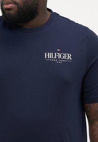 Granatowa koszulka z krótkim rękawem wykonana z bawełny, z białym logo "HILFIGER NEW YORK 1985" na piersi oraz małym akcentem logo powyżej.