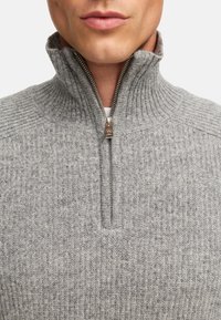 Maglione grigio a costine con colletto alto e chiusura a mezza zip. Presenta una texture liscia e sottili variazioni di tonalità.