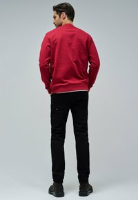 Pull rouge à col rond, associé à un jean noir et des bottes sombres. Le tissu semble texturé et est légèrement ajusté.