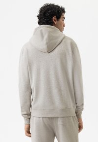 Felpa grigia chiara realizzata in tessuto morbido, con un grande cappuccio, polsini e orlo a costine, dal taglio casual e una texture liscia.