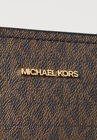 Brun tekstureret læderpunge med et guld "MICHAEL KORS" logo, der har et diskret mønster og glatte kanter. Kompakt design, minimal hardware.