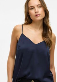 Granatowa satynowa koszulka na ramiączkach z cienkimi spaghetti i dekoltem w kształcie litery V, prezentująca gładką, błyszczącą teksturę oraz luźny krój.