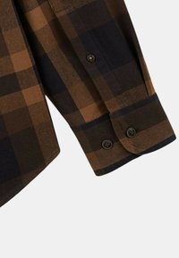 Chemise à carreaux marron et noir avec des manches à poignets boutonnés, texture douce et coupe droite. Le tissu présente des carreaux contrastés.