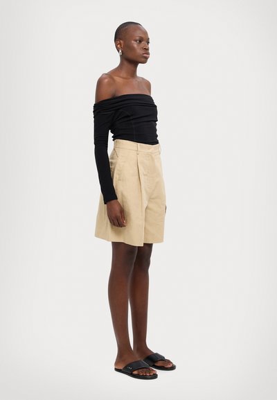 Sort off-shoulder top med lange ærmer, beige plisserede shorts og sorte slidesandaler. Glat stof og neutral farvepalet.