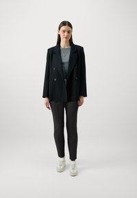 Dobbeltrøyd svart blazer, grå skjorte, svarte slim-fit bukser og hvite sneakers. Minimalistisk design med en glatt tekstur.