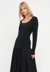 Melnas ilgas piedurknes krekls ar apaļu izgriezumu. Izgatavots no mīkstas auduma, centrā ir neliels balts logo. Slim fit (apvērsts) dizains.