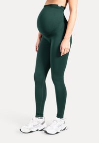 Höghöga gröna leggings gjorda av elastiskt material, med en slät yta och en figurnära design, lämpliga för gravidkläder.