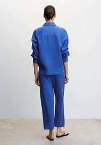 Chemise en lin bleu et pantalon assorti, coupe décontractée. La chemise est dotée d'un col et de manches retroussées. Le pantalon a une coupe droite et une longueur cheville.