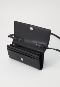 Portafoglio in pelle nera con una texture liscia, dotato di chiusura a scatto, diverse tasche per carte e una sezione con zip all'interno.