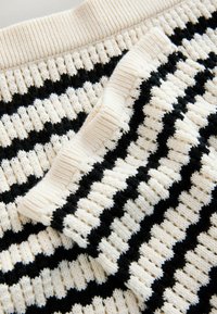 Tissu tricoté crème et noir avec poignets et col côtelés présentant des rayures horizontales alternées.