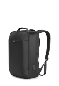 Mochila negra con material de nailon suave, forma rectangular, correas de hombro acolchadas y un pocket frontal con cremallera. Presenta un logo en la parte delantera.